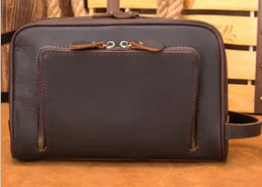 Dark brown genuine leather designer handbag, rectangular clutch style with front zipper pocket and wrist strap.