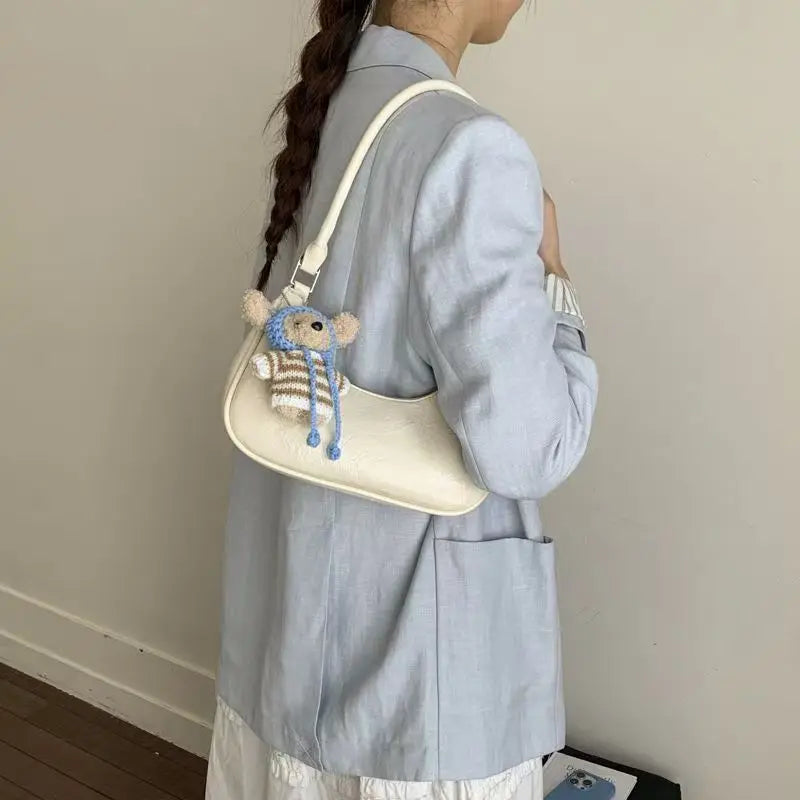White leather dumpling shoulder bag with cute bear charm. Waterproof crescent handbag for women, chic trendy style.