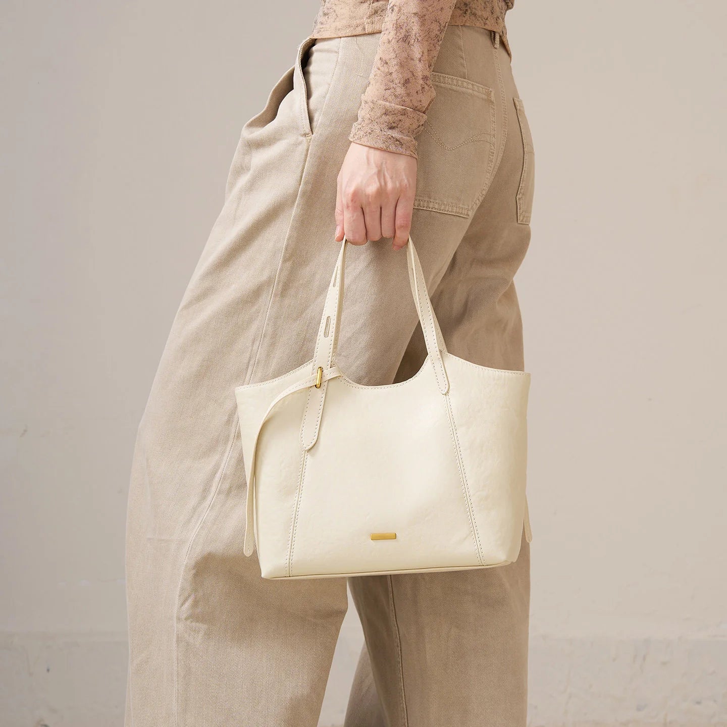 Cream genuine top grain leather designer handbag with minimalist gold hardware and sturdy twin shoulder straps.