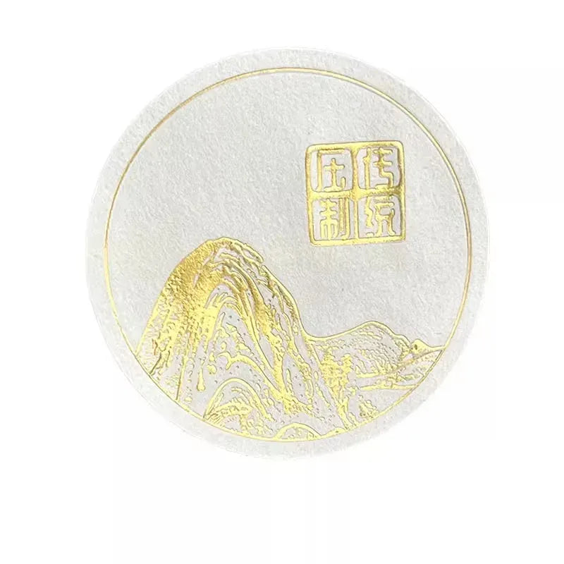 White round sticker label with gold mountain and seal logo, embossed.
