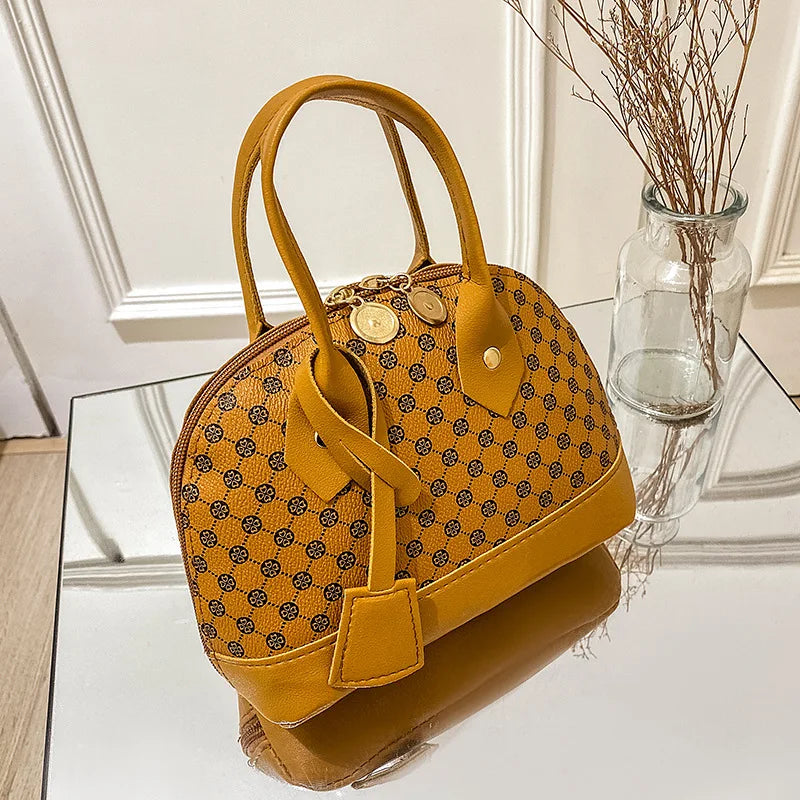 Mustard yellow designer shell handbag with black clover pattern, top handles, zipper closure, and gold hardware.