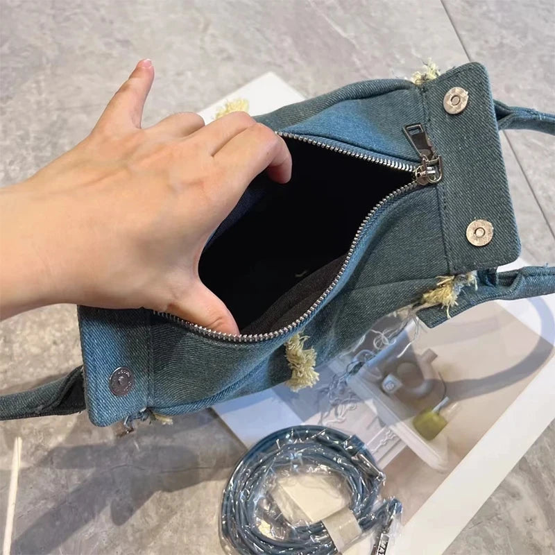 Small vintage blue denim hobo bag with frayed edges, silver zipper, metal studs, and detachable crossbody strap.