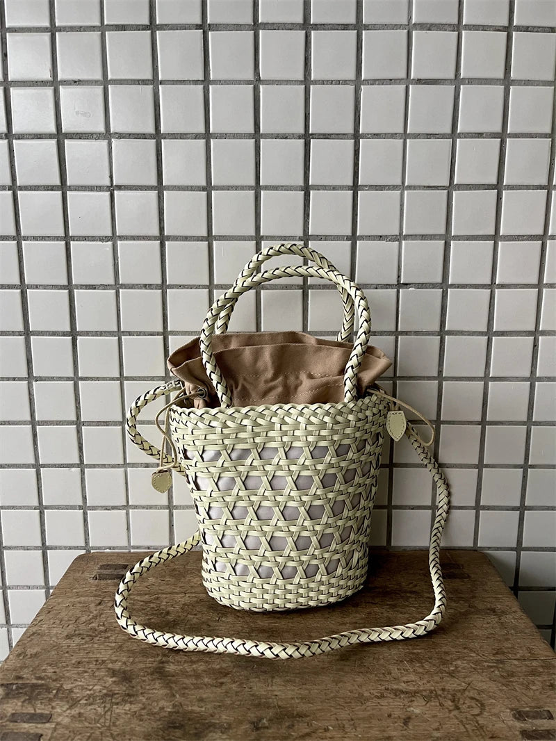 Cream handwoven leather bucket bag with cross-weave cannage design, braided handles, and tan fabric drawstring insert.