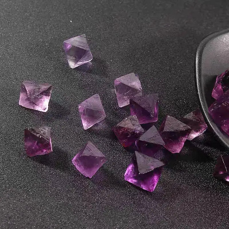 Purple rough crystal octahedra scattered on dark surface, several small pieces and spoon