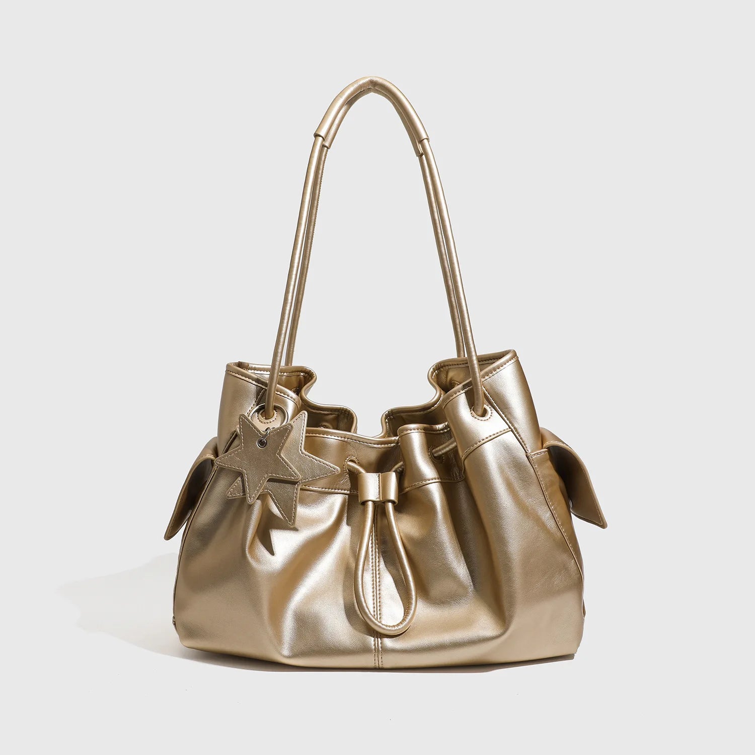 Metallic gold slouchy shoulder bag with drawstring, star charm, and double handles. Luxury designer commuting handbag.