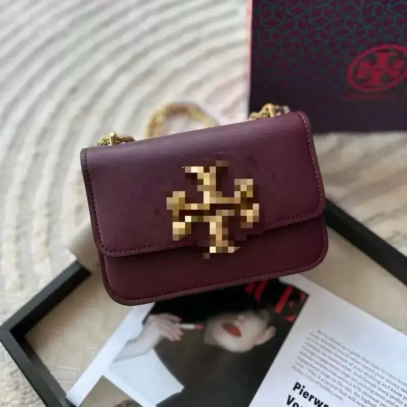 Maroon leather crossbody trunk bag with gold metal logo, chain strap, and structured rectangular design.