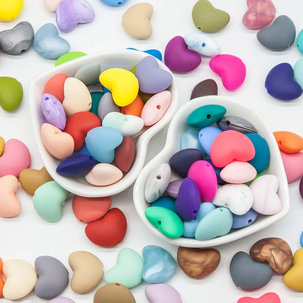 Multicolor silicone heart beads for baby teething toys in heart-shaped bowls.