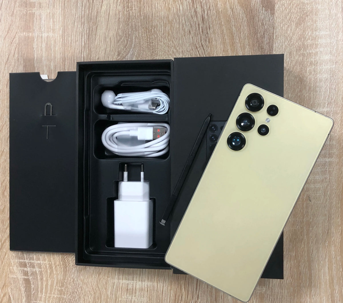 Gold smartphone with quad rear cameras, in box with charging cable and wall adapter