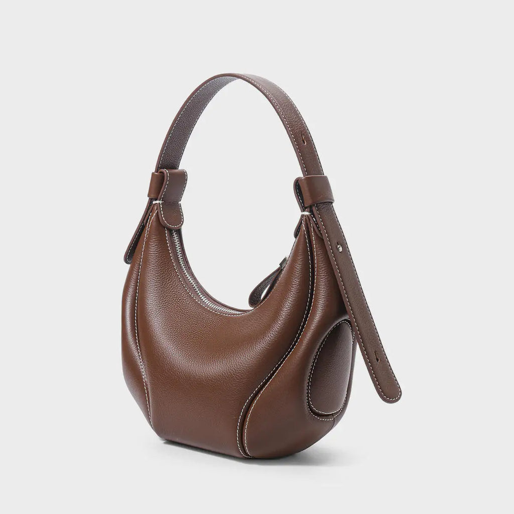 Brown leather half-moon crossbody handbag with contrast white stitching and adjustable strap. Luxury trunk-style design.
