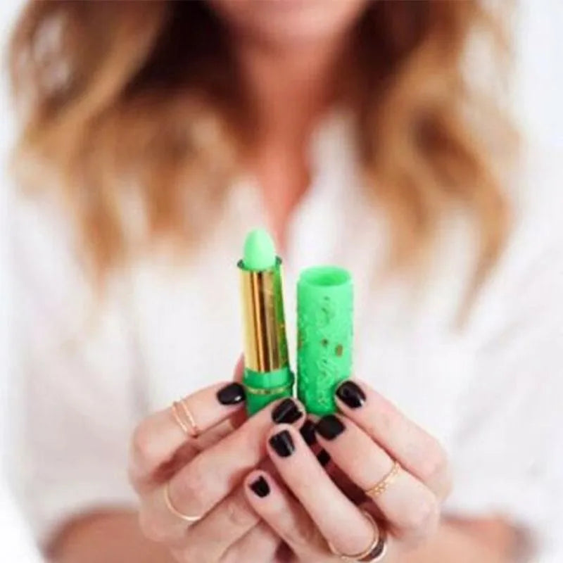 Green magic color-changing lipstick in a gold tube, held by woman with black nails. Long-lasting lip makeup, 6pcs set.