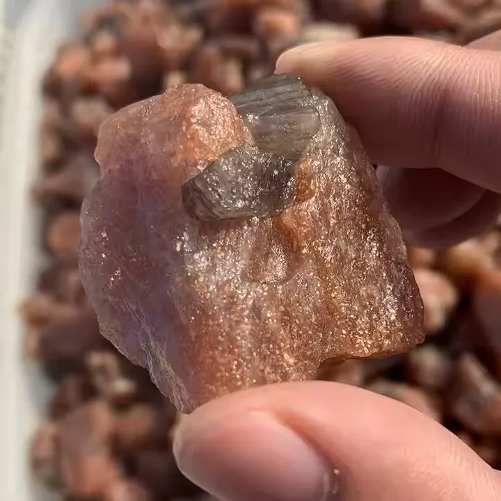 Rough sunstone quartz crystal with glittery surface, held between fingers