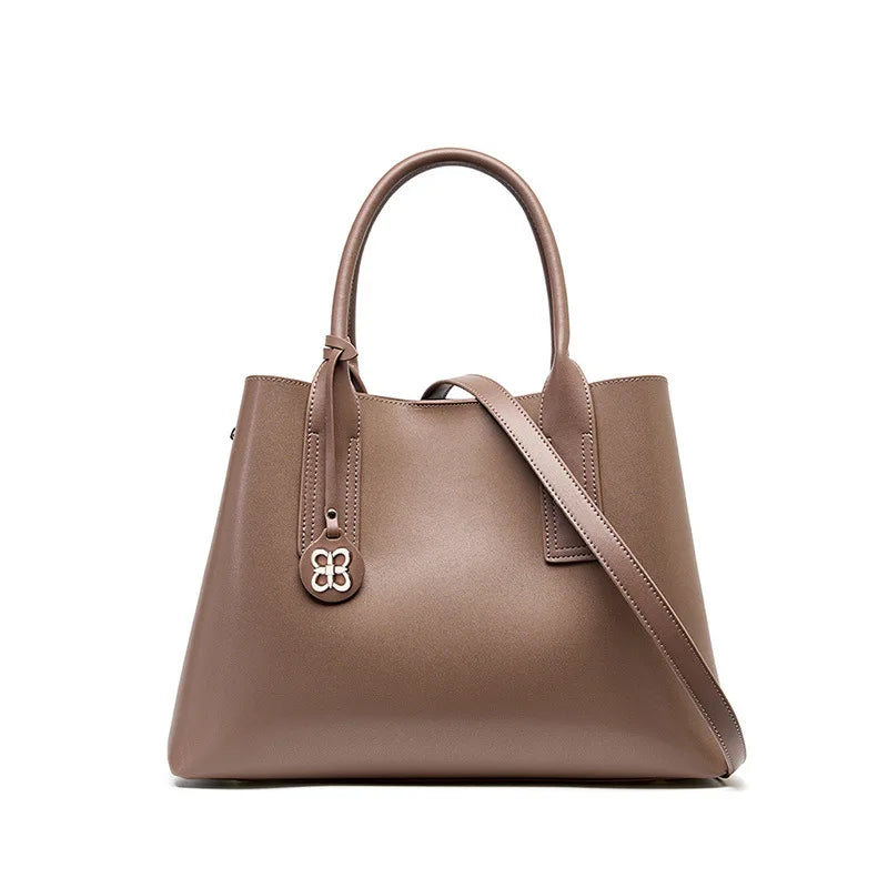 Taupe genuine leather designer handbag, elegant tote with removable crossbody strap and clover charm accent.