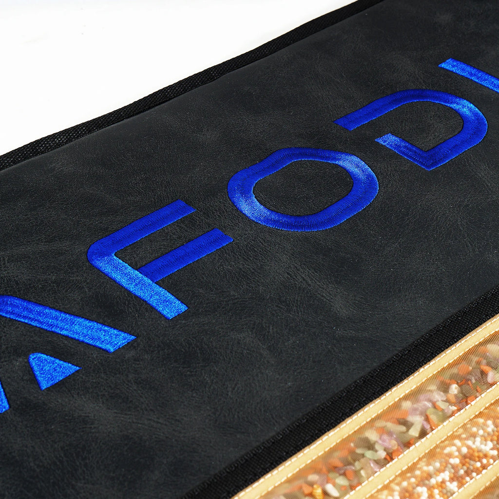 Black leather heating pad with blue embroidery and a mesh section filled with small, colorful therapy stones.