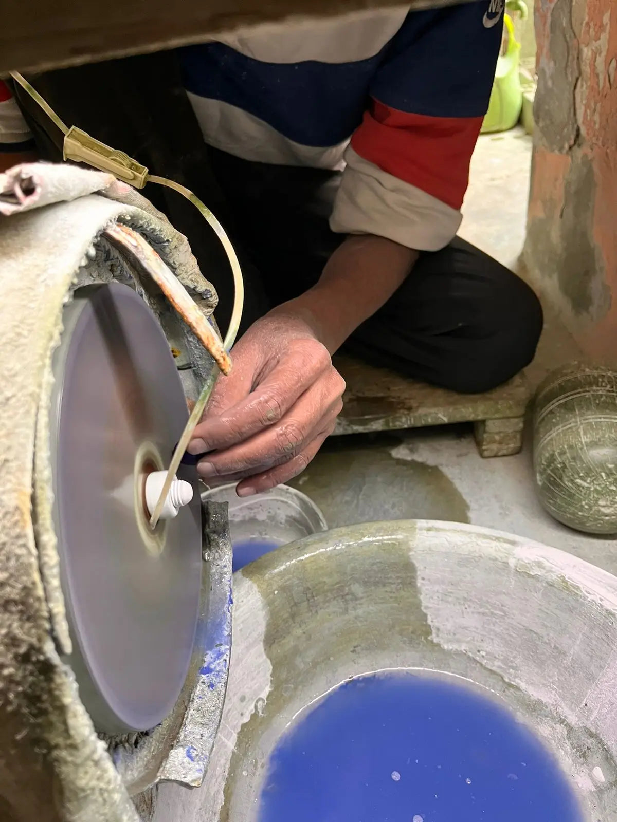 Polished rough gemstone being ground on a blue wheel, held by hand