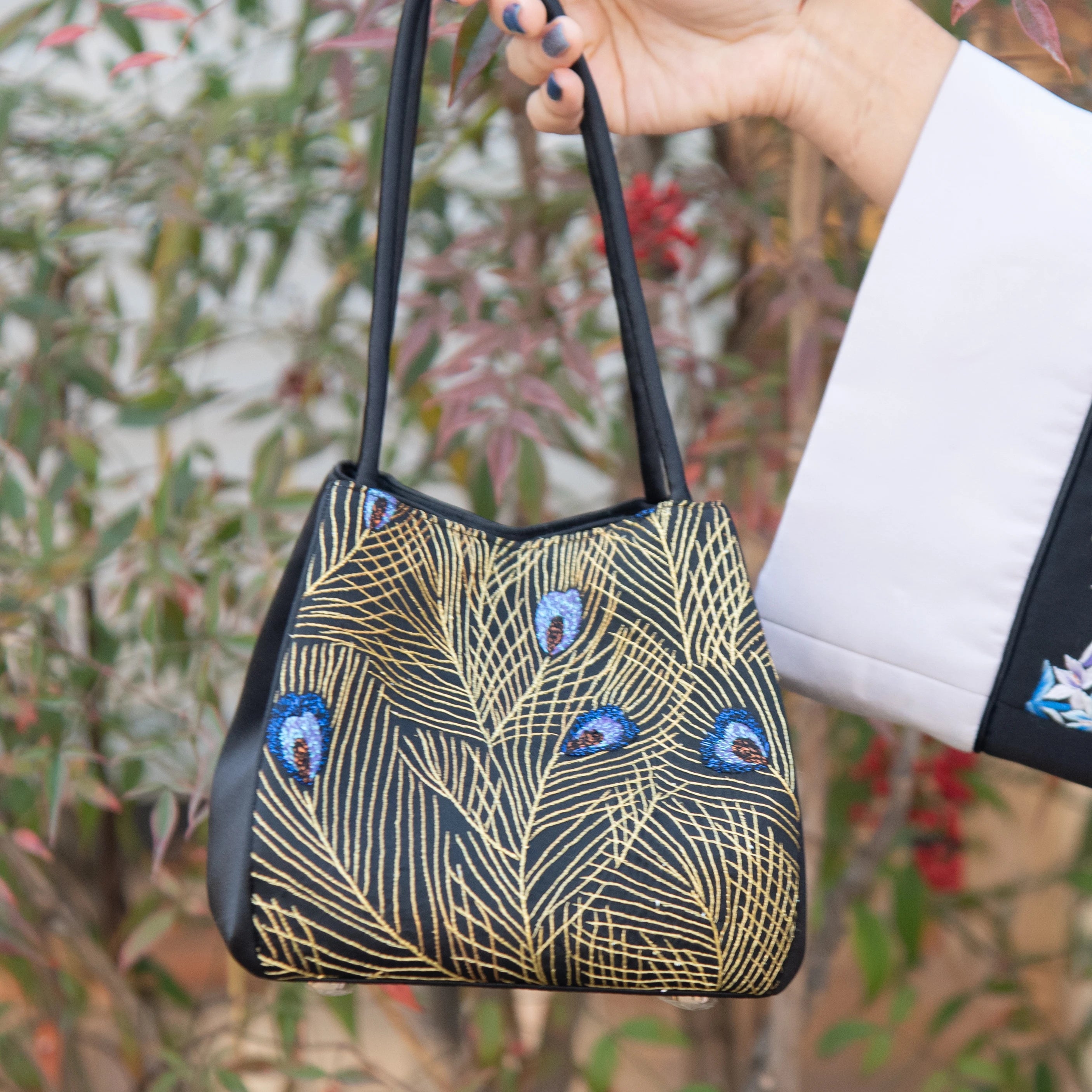 Luxury artisanal black trunk handbag with gold metallic peacock feather embroidery and beaded blue accents.