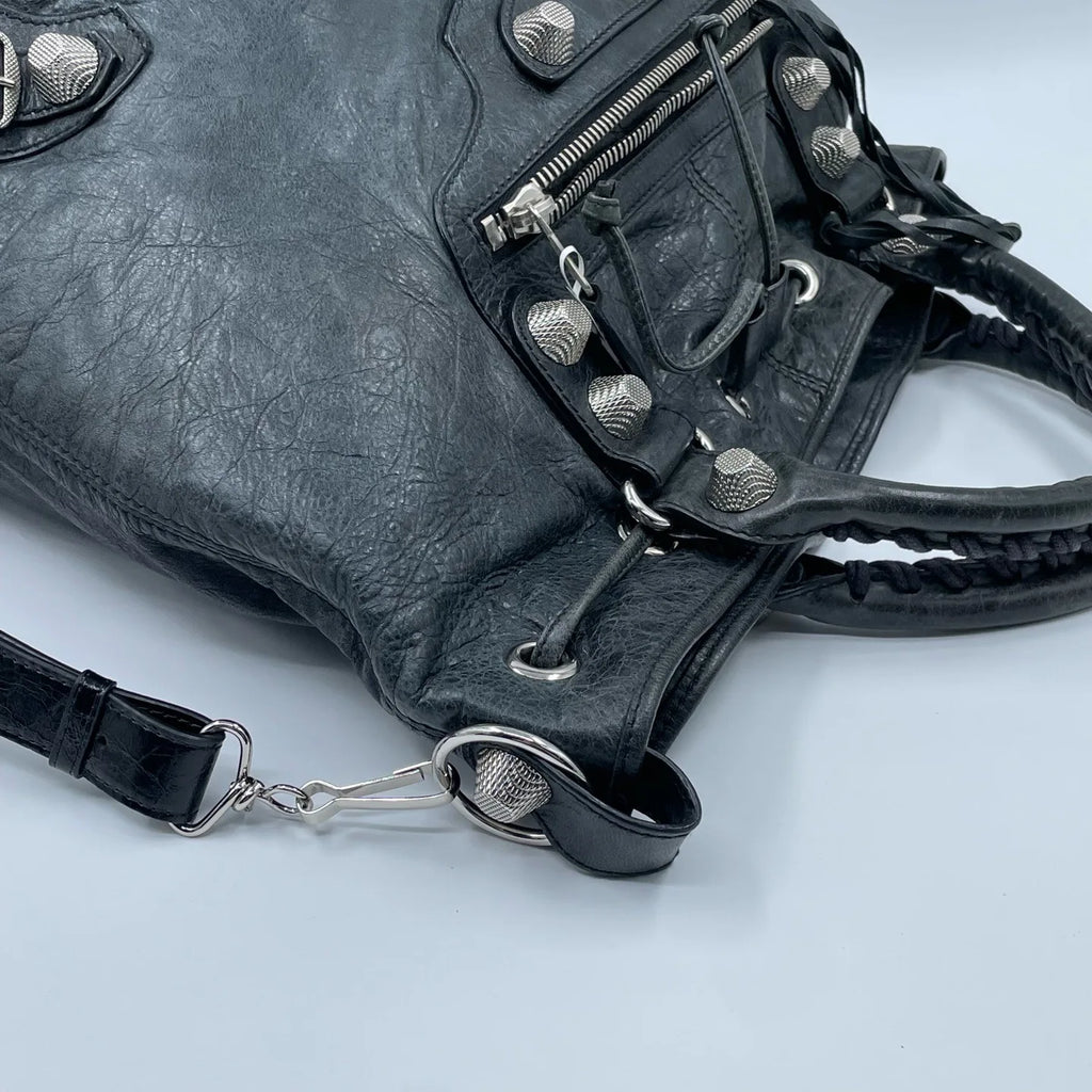 Pre-owned black leather designer bucket bag with silver metal studs, zippered pocket, and braided top handle.