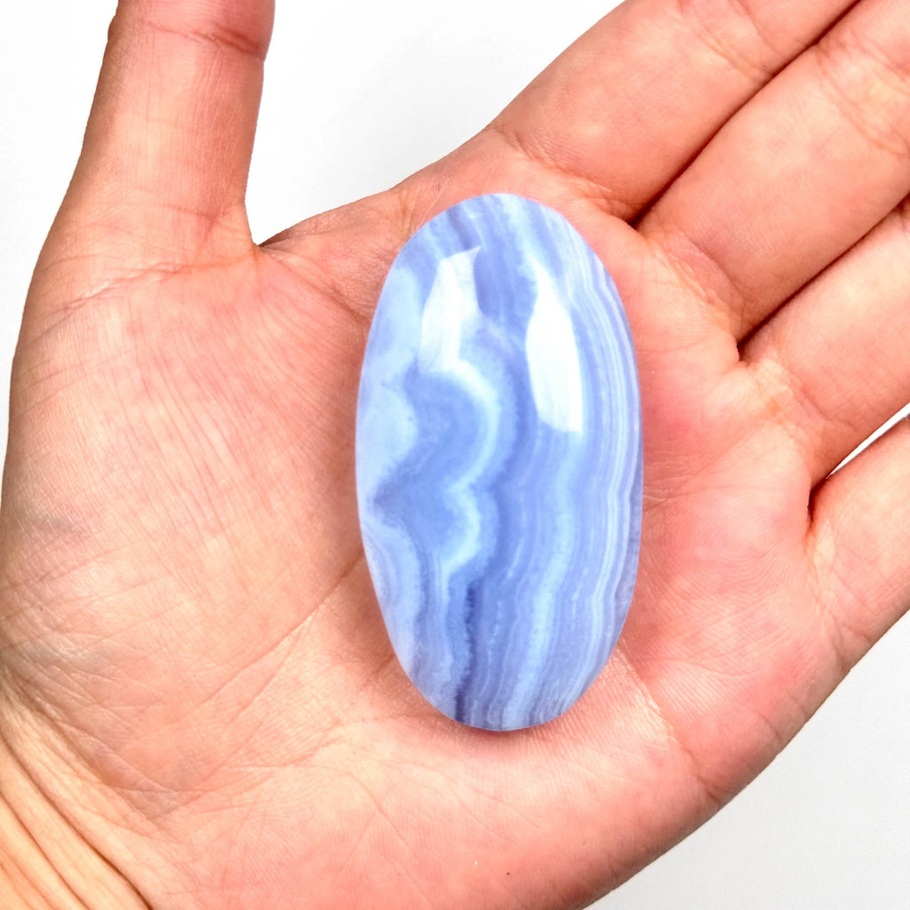 Single blue lace agate palm stone in an open palm, smooth oval with white-blue wavy stripes
