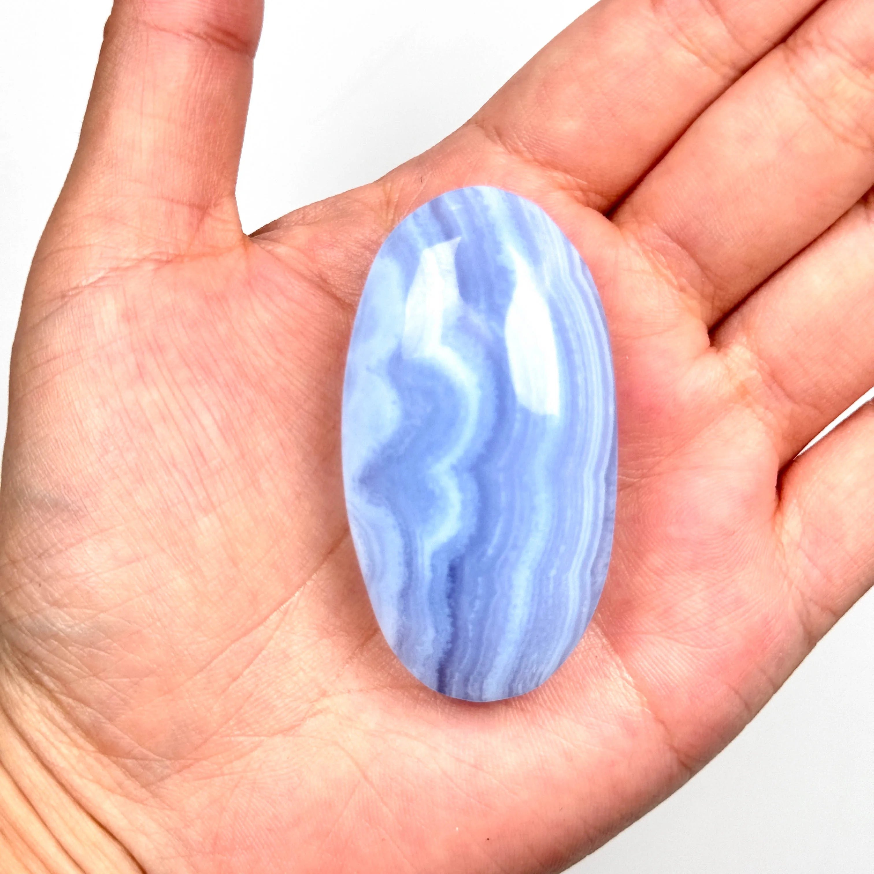 Single blue lace agate palm stone in an open palm, smooth oval with white-blue wavy stripes