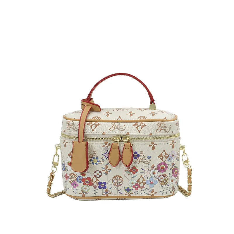 Designer vanity trunk bag in cream cowhide leather with multi-color flower monogram and gold chain crossbody strap.