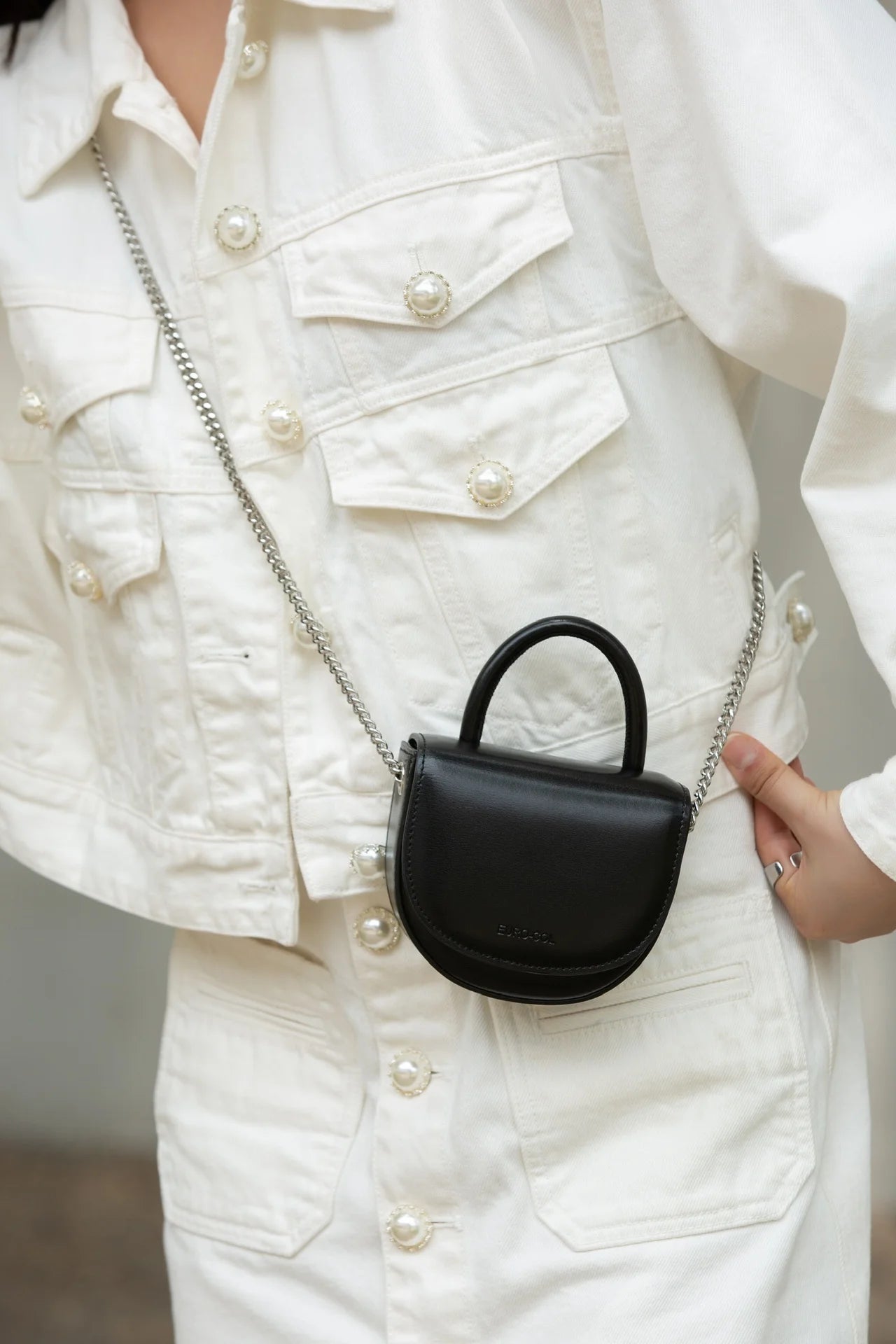 Black cowhide leather mini clutch with silver chain strap, round top handle, and designer style for evening wear.