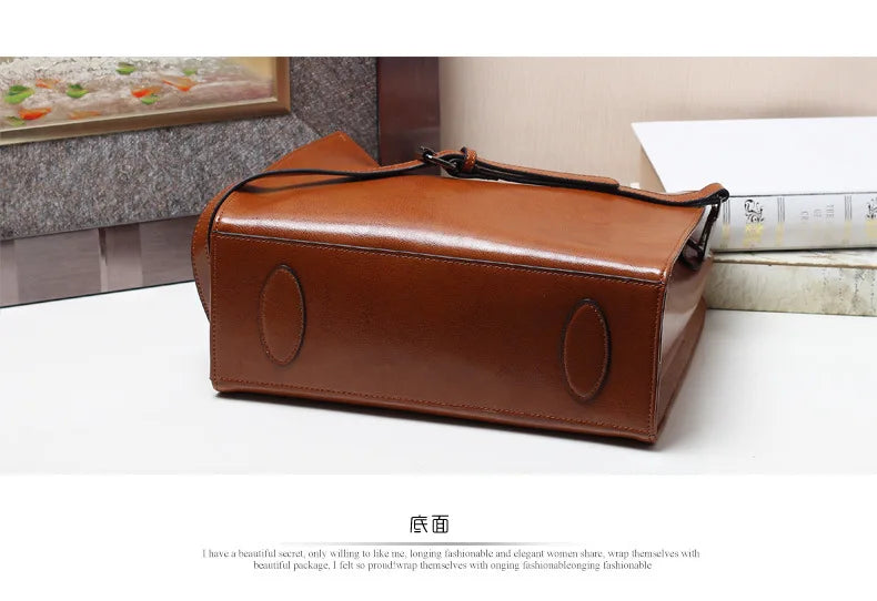 Tan genuine leather trunk handbag, classic structured design with protective base studs and shoulder strap.