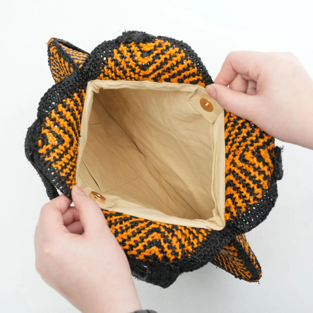 Black and orange boho crochet tote bag with fabric lining and gold snap button closure. Top view of summer handbag.