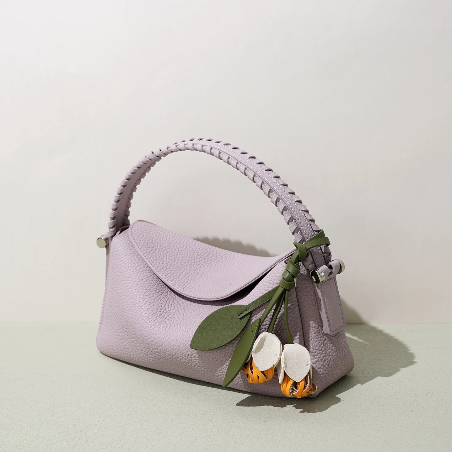 Lilac leather crossbody bag with braided handle and cute floral charm. Designer style small handbag for women.