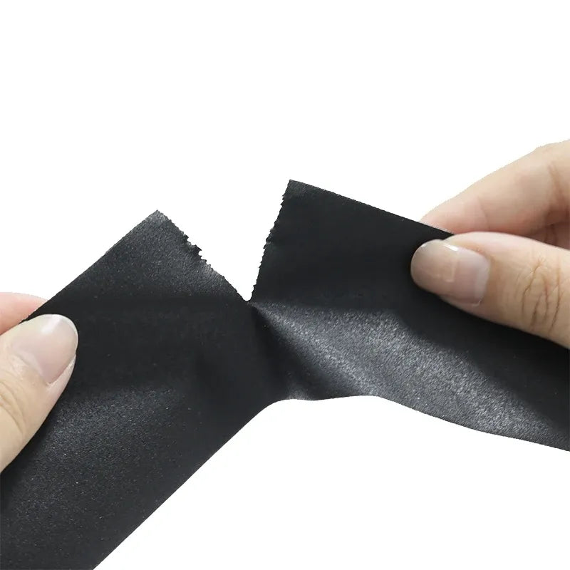 Hand pulling a strip of black matte gaffer tape with textured cloth surface