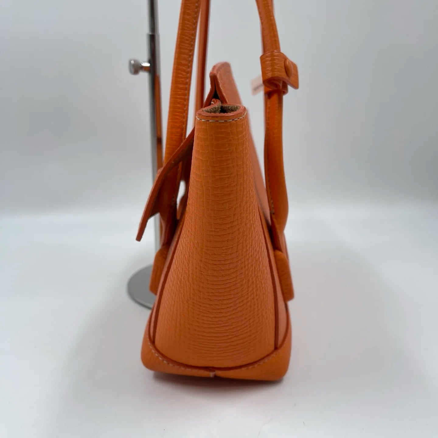 Luxury orange genuine leather designer handbag, textured tote style with two handles and flap closure.