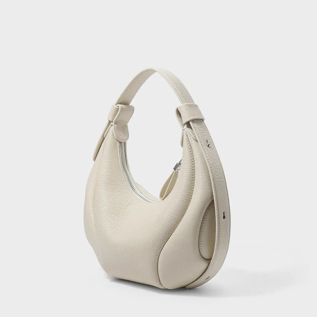 Beige pebbled leather half moon crossbody bag with structured side panels and zip closure for luxury minimalist style.
