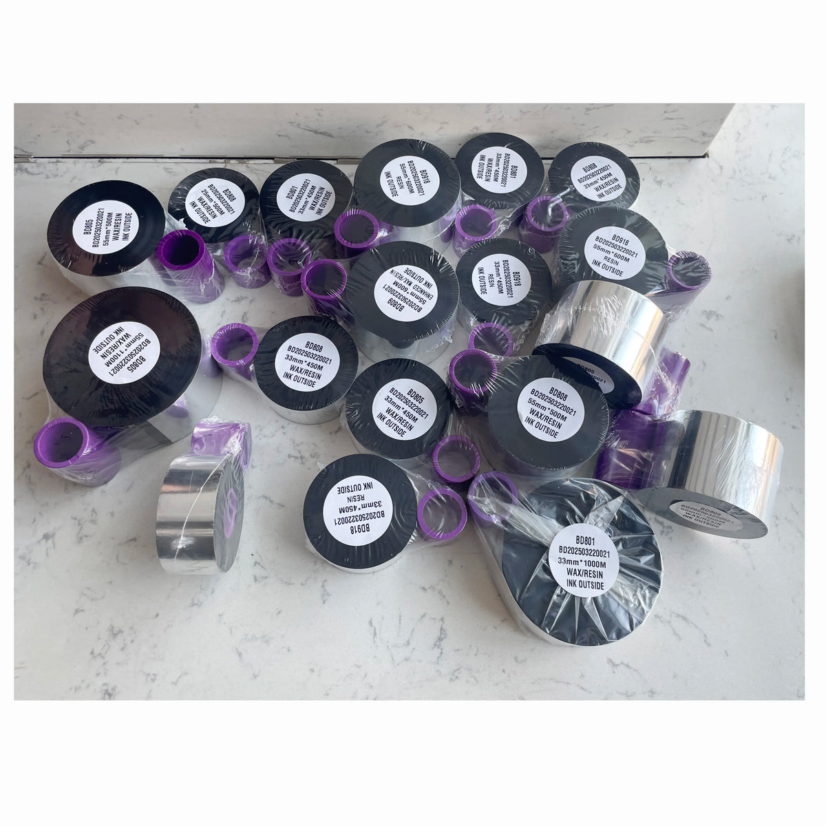 Assorted black thermal transfer ribbon rolls with purple cores and product stickers