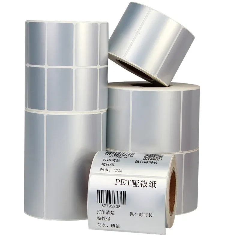 Thermal matte silver PET label rolls with barcode labels, stacked and partially peeled