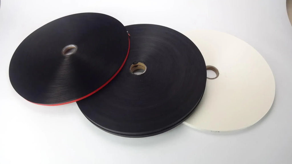Spool of black thermal label paper tape and matching roll on a white backing card.