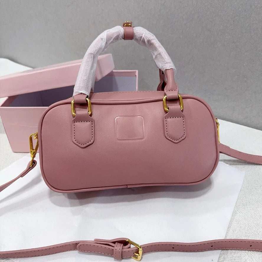 Dusty pink leather luxury trunk handbag with gold hardware, top handles, and an adjustable crossbody strap.