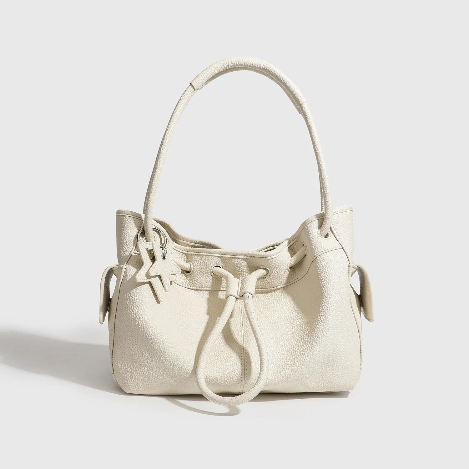 Cream pebbled leather shoulder bag, niche design with drawstring closure, star charm, and spacious commuting style.