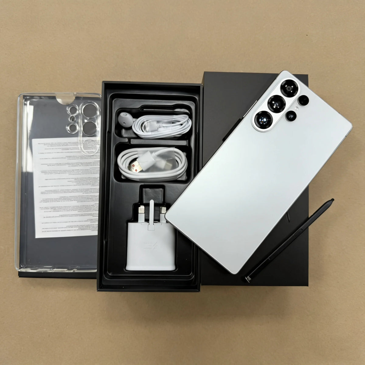 Unlocked smartphone with white back, shown beside open box with cables and adapter