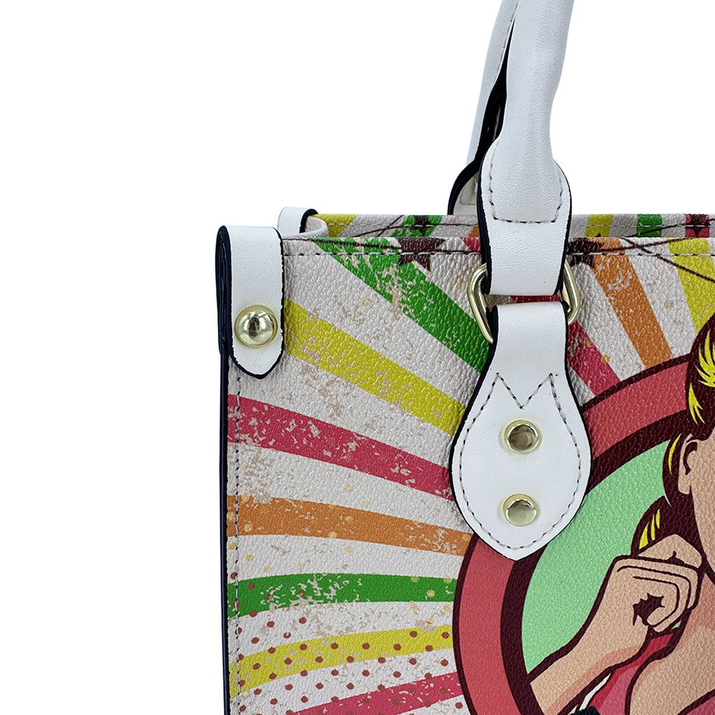 Small faux leather trunk handbag with colorful vintage pop art print, white handles, and gold hardware accents.