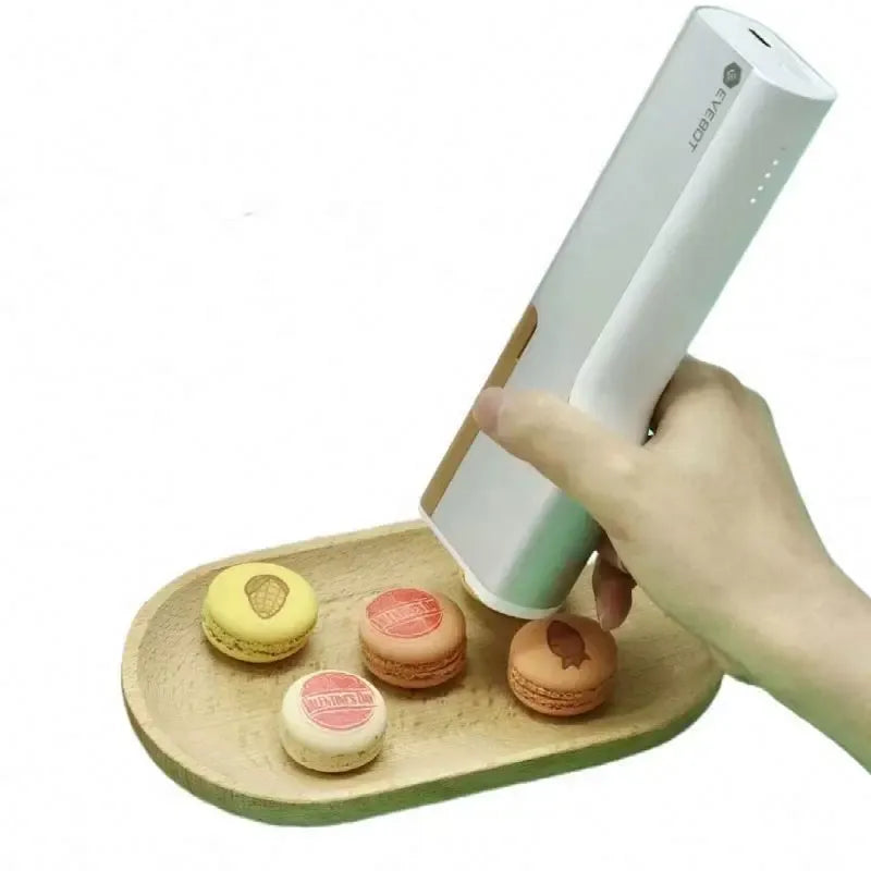 Handheld food inkjet printer pen in white, held above macarons for edible printing
