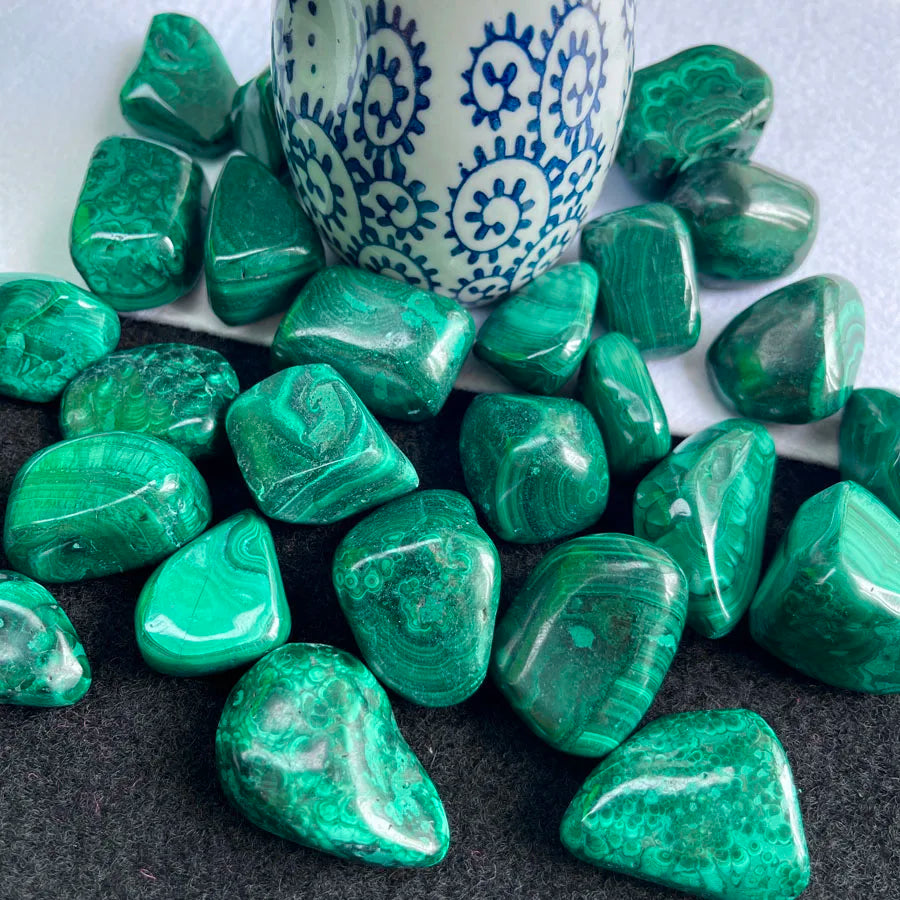 Tumbled malachite stones in a white ceramic cup, glossy dark green teardrops