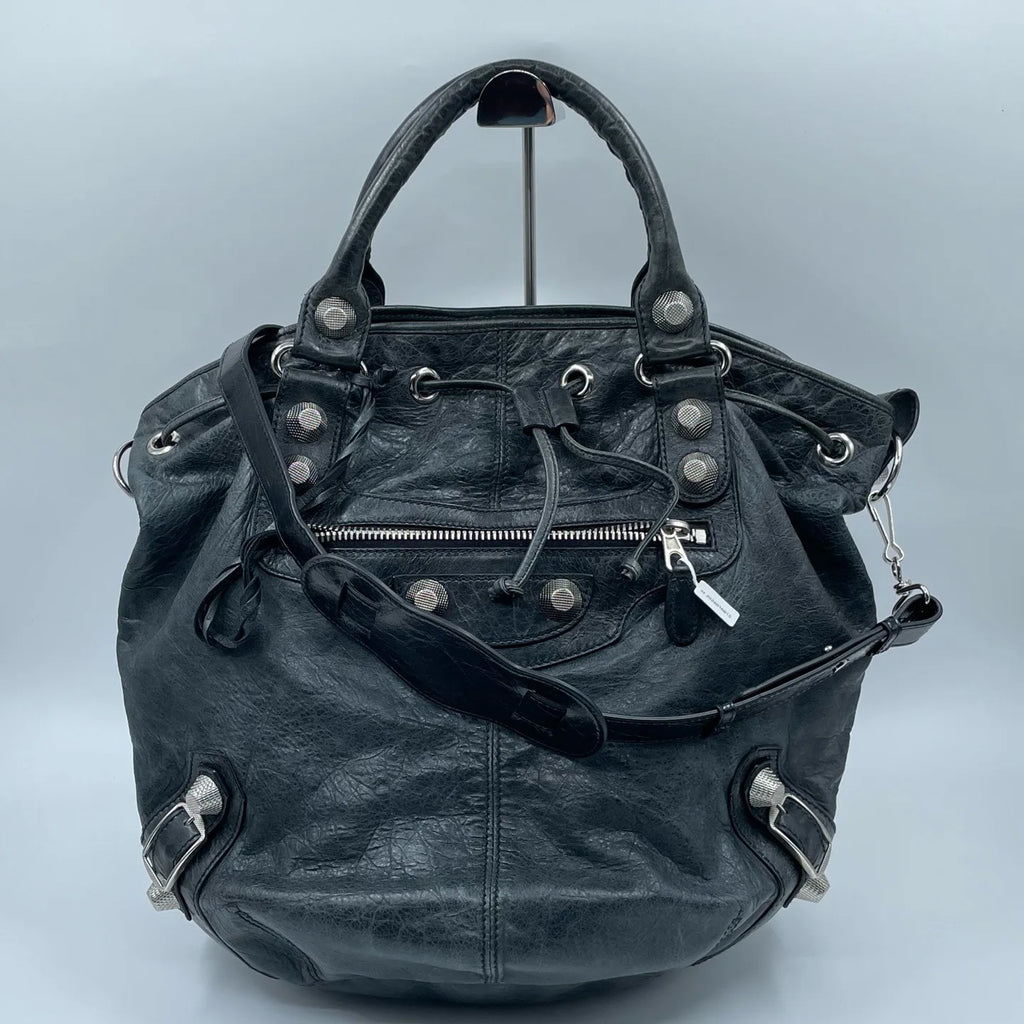 Pre-owned black leather designer bucket bag with metal studs, top handle, zip pocket, and adjustable shoulder strap.
