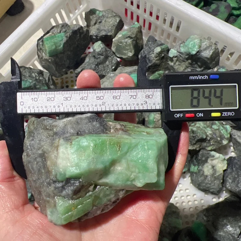 Rough green crystal quartz chunk beside a measuring caliper, mint-green on dark matrix