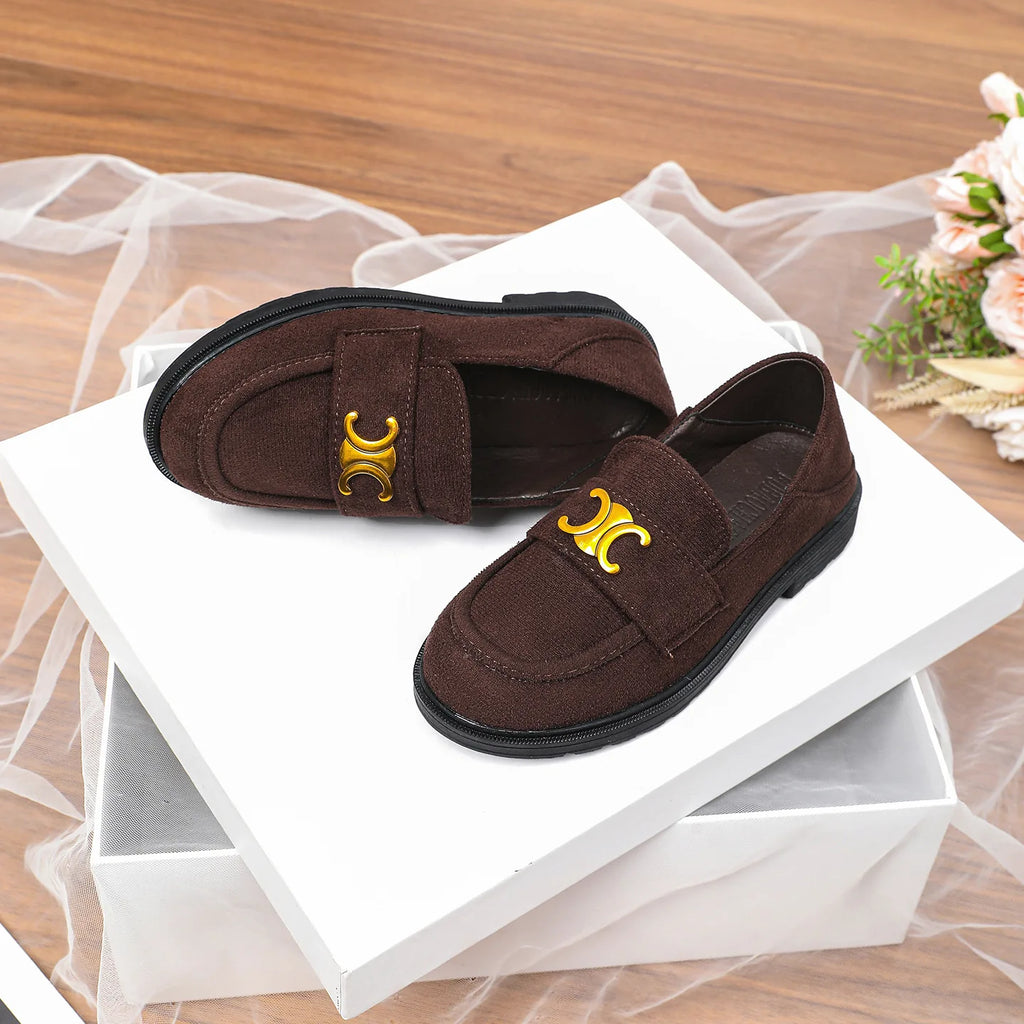 Luxury brown suede loafers with gold logo hardware and black rubber lug soles on a white pedestal box.