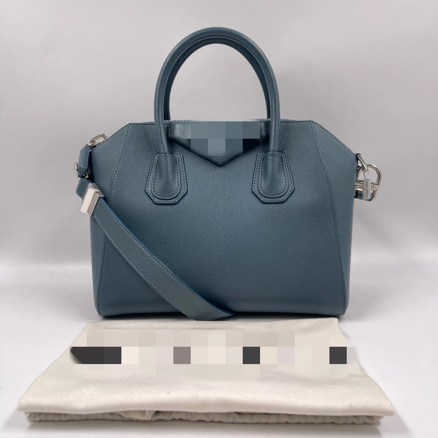 Blue genuine leather designer tote bag with top handles, crossbody strap, and classic structural trapezoid shape.
