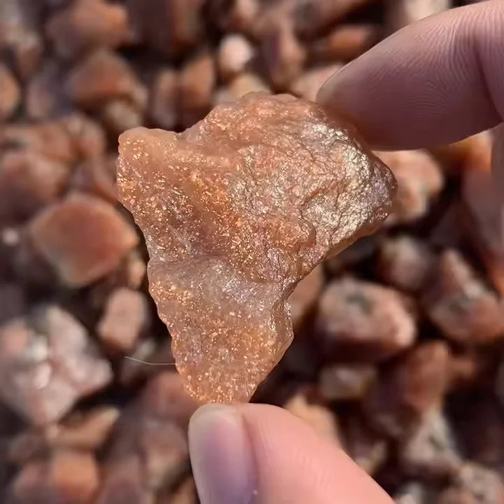 Rough golden sunstone quartz crystal specimen, held between thumb and fingers