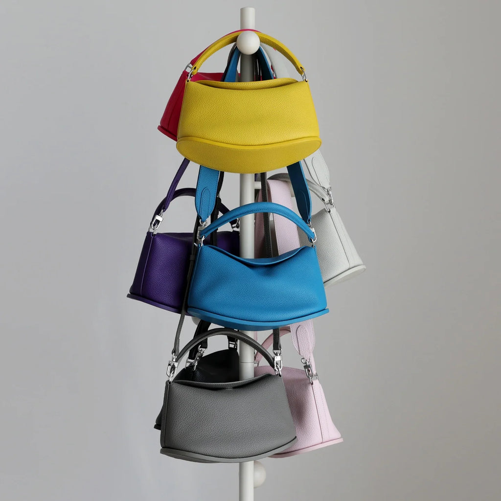 Colorful leather pillow handbags hanging on a rack. Designer cowhide commuting purses with dual straps and magnetic closure.