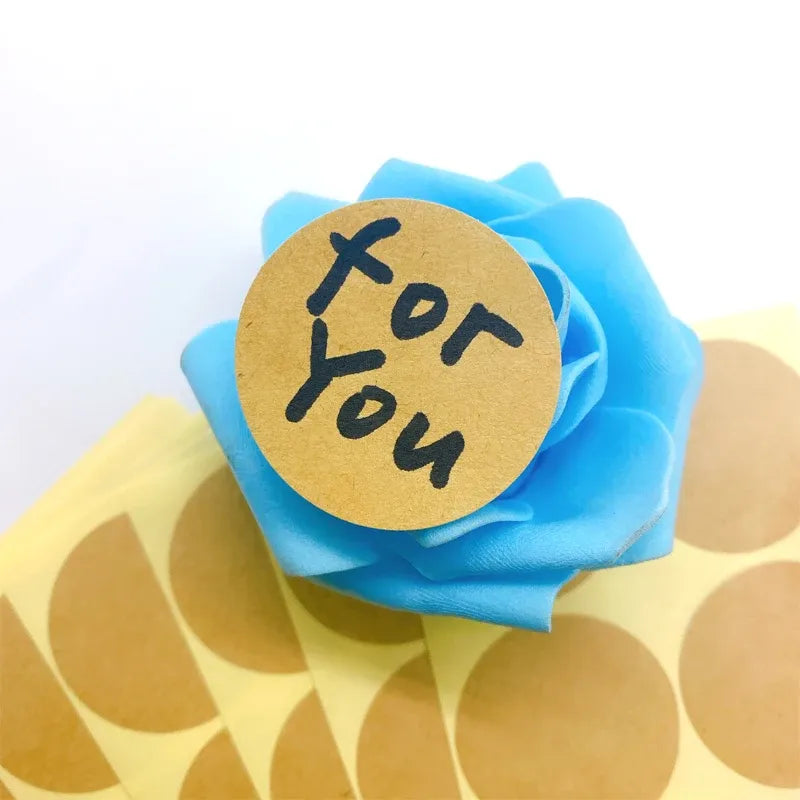 Round kraft paper sticker with printed doodle-style face and handwritten text label