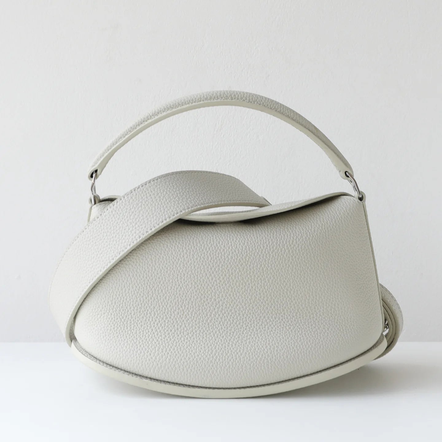 Off-white pebble-grain cowhide leather designer handbag, pillow-shaped with dual straps and magnetic closure.