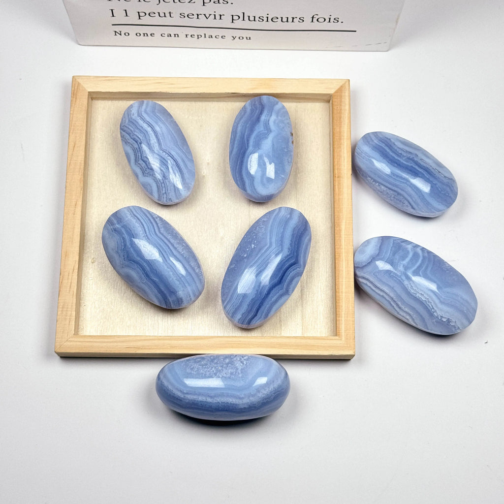 Blue lace agate palm stones in a wooden display tray, smooth ovals with blue banded patterns