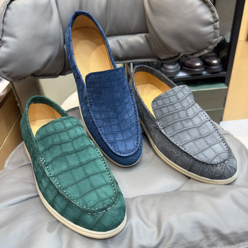 Luxury men's crocodile-embossed suede loafers in blue, green, and grey with flat white soles and slip-on style.