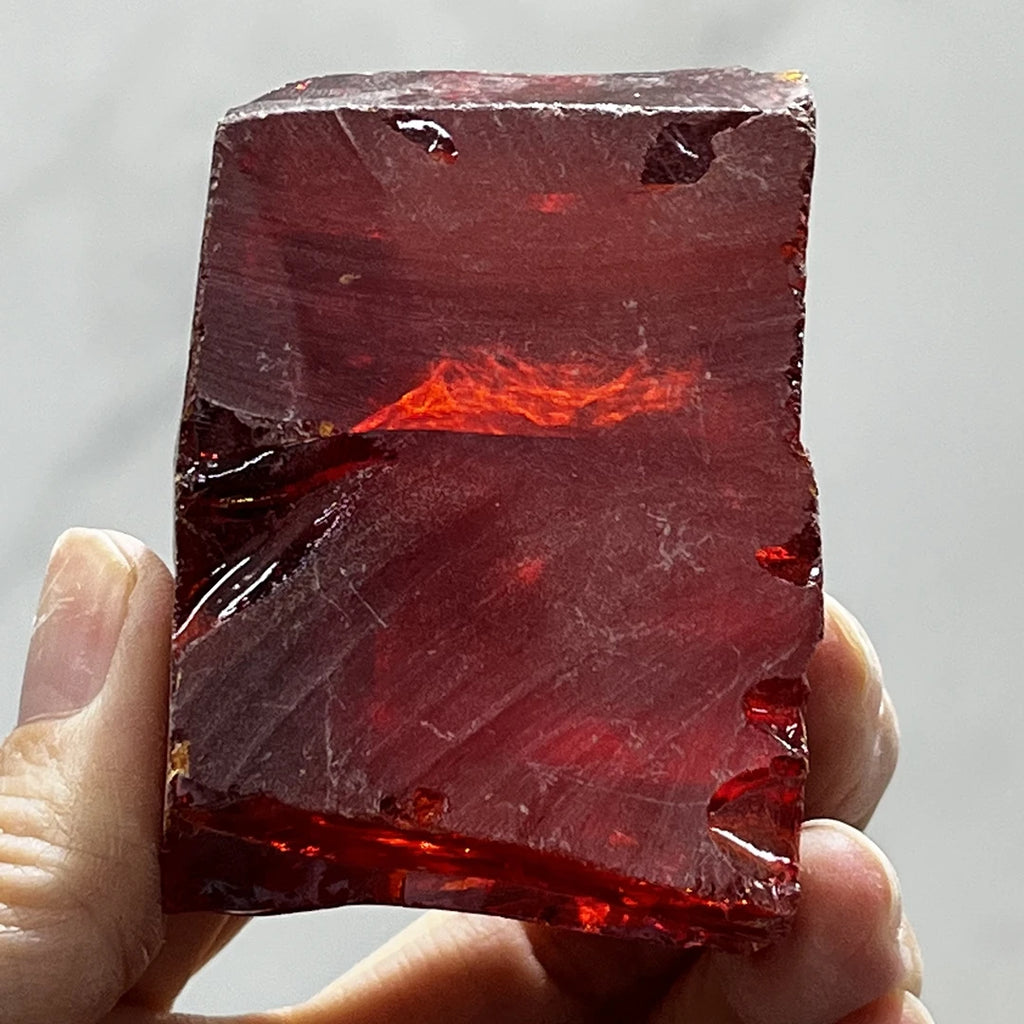 Loose red rough cubic zirconia slab, uncut faceted with glowing red highlight, held